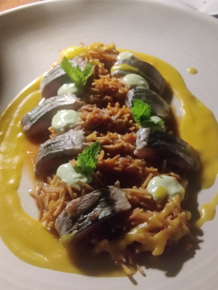Pieces of almost raw mackerel on a bed of super small pasta that looks like rice, called fideo. Sprigs of mint poke out of the dish which is surrounded by a yellow sauce
