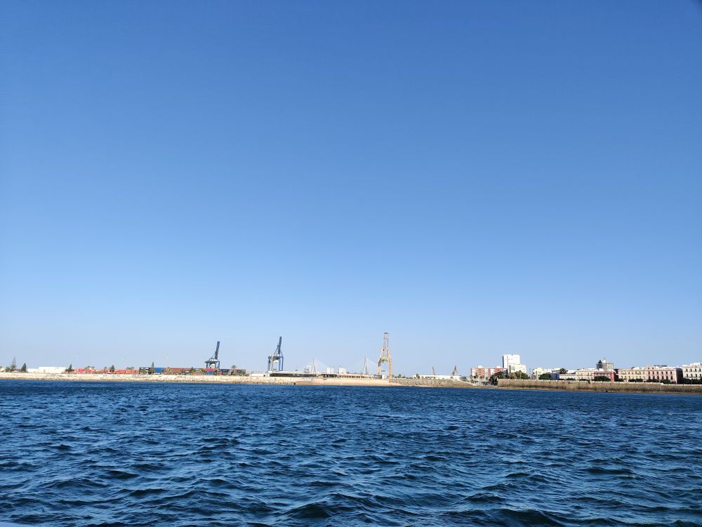 A thin sliver of harbour in-between the sky and the sea. Cranes used to load shipping containers stand over the harbour and kinda look like giraffes 