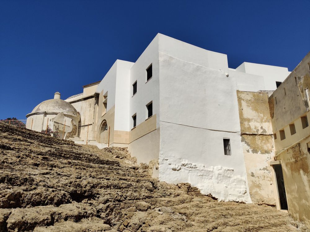 White buildings flank the theatre seating.

The Moors filled in the theatre with sand, stones and debris and the exact location of the theatre was unknown until about 30 years ago during excavations for some new buildings planned for the site. Those were never built and instead archeologists spent 20+ years excavating about 1/3 of the theatre seats and stage.

Apart from a few chunks of columns, the stones used to build the upper part of the theatre haven't been found