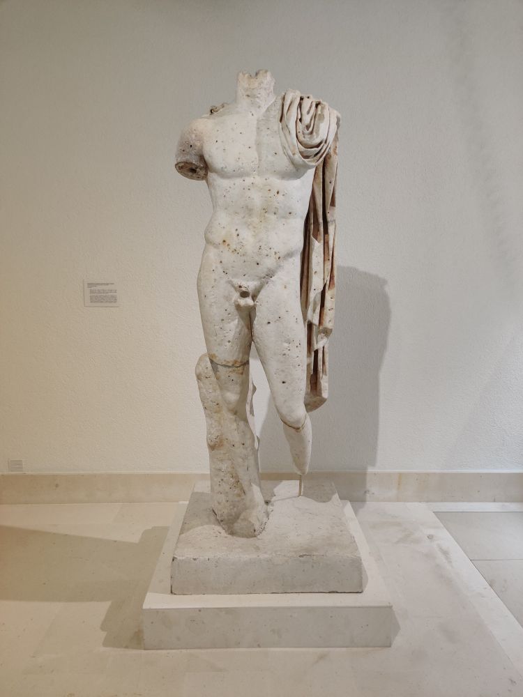 A typical statue of a muscular, naked Roman man with a robe draped over his left shoulder. His head, arms, left foot and penis are missing 