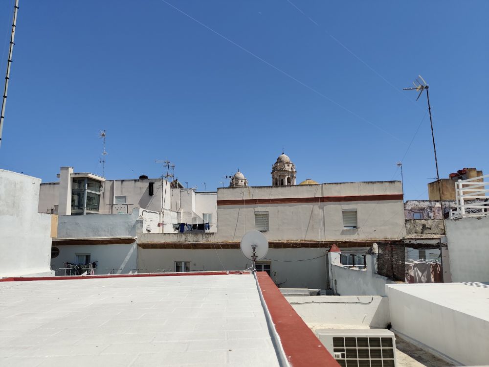 A jumble of typically Mediterranean house rooftops with the towers from merchant houses in the background. Stripes of terracotta tiles lined some of the roofs and buildings. Many of the houses have TV antenna 