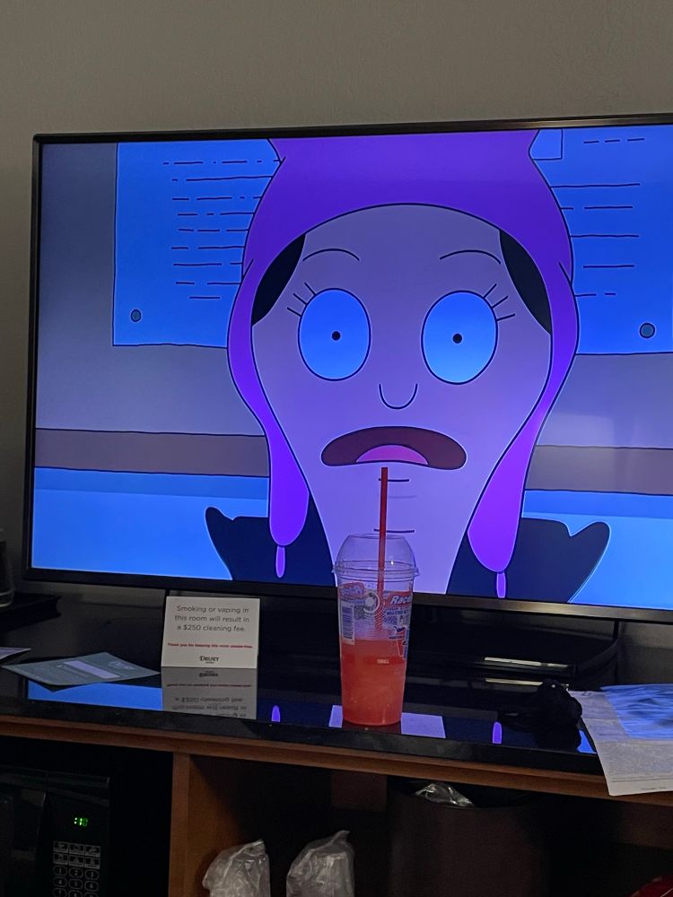An image of a slushy drink sitting in front of a hotel tv. The slushy is lined up to look like Louise from Bob’s Burgers is taking a drink.