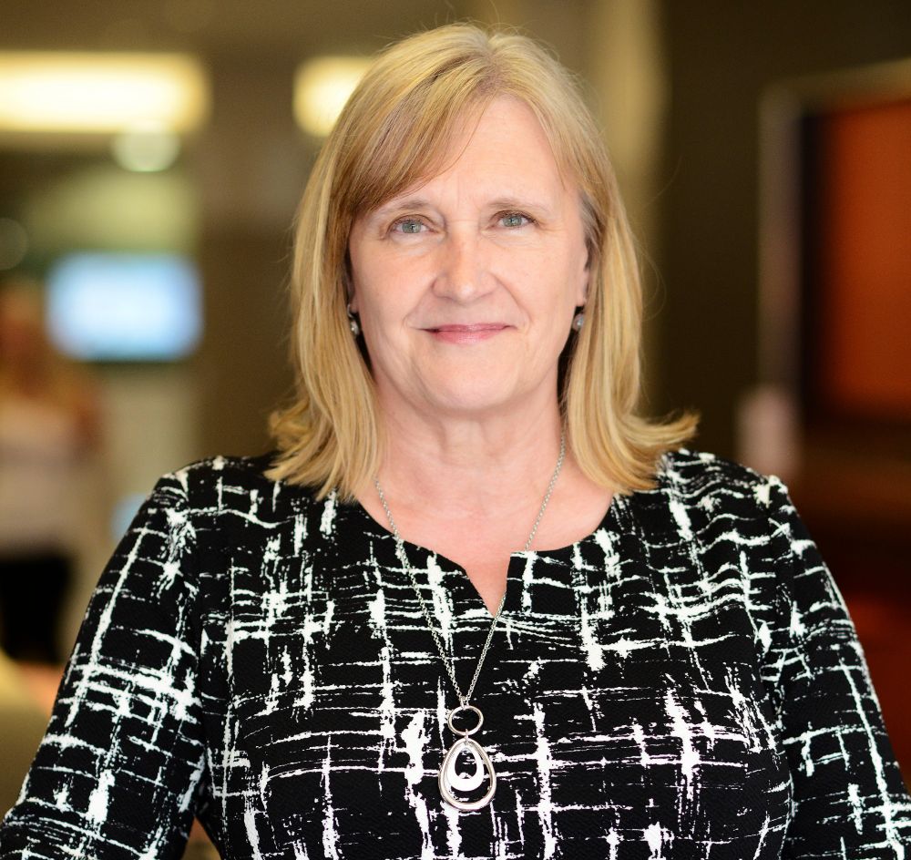Sue Farrington is wearing a black and white top. She is smiling and looking directly at the camera.