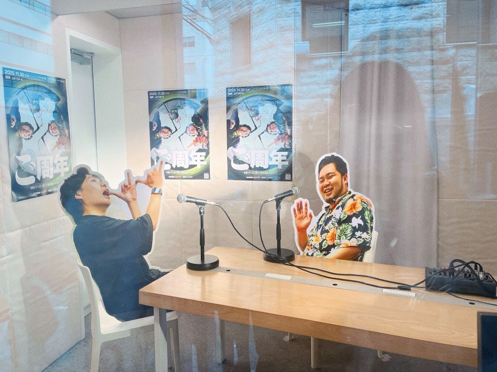 ブースを外側から撮影した写真です。ブース内には長机とマイクが2本あり、くるまさんとケムリさんの等身大パネル（？）が飾られています。