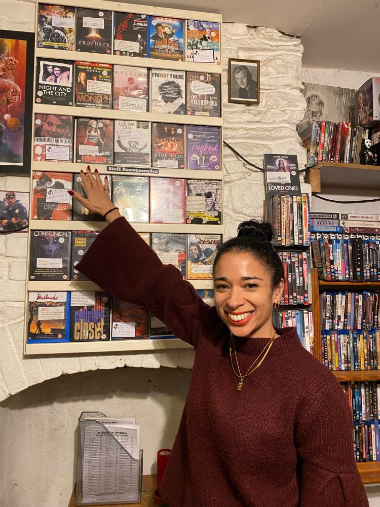 Ellen E Jones standing in front of a ‘Staff Recommends’ DVD display at 20th Century Flicks in Bristol, UK, the world’s longest continuously running video rental shop.