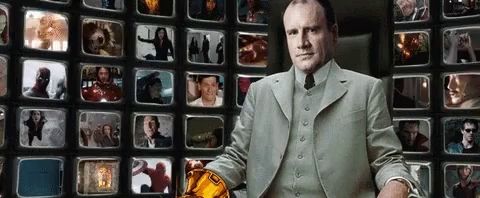 a man in a suit and tie is standing in front of a wall of television screens