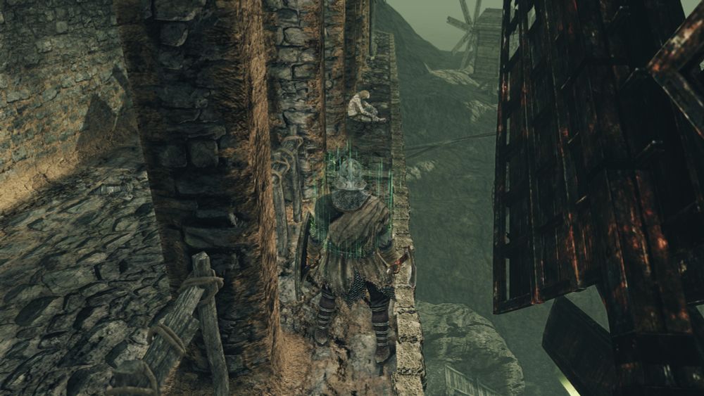 Screenshot from Dark Souls 2 of a pale-skinned NPC sitting on a ledge near a burned windmill.