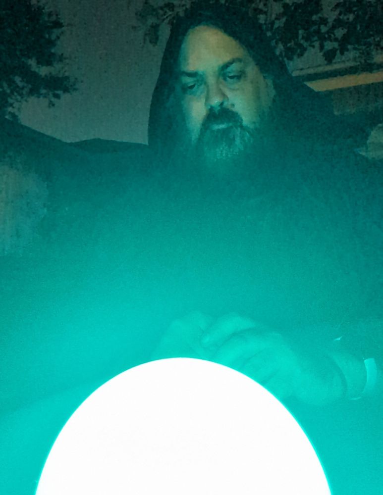 A man dressed as a wizard gazes into a blue glowing orb.