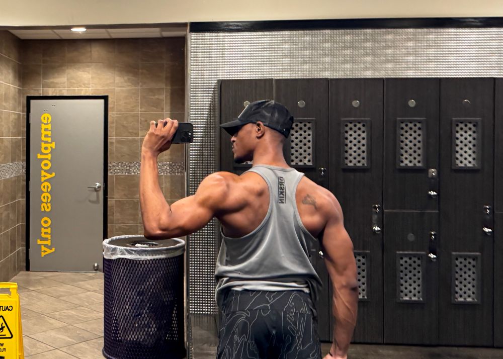 Antoine (the Designer Baddie, Backshot Daddy, Secretary of Wide Spreads), flexes his back muscles in a grey tank top. He’s very proud of his progress. 