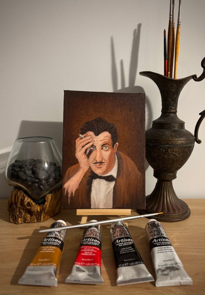 A photo of a small oil painting of Vincent Price. In front of the canvas are the paints and brush used.