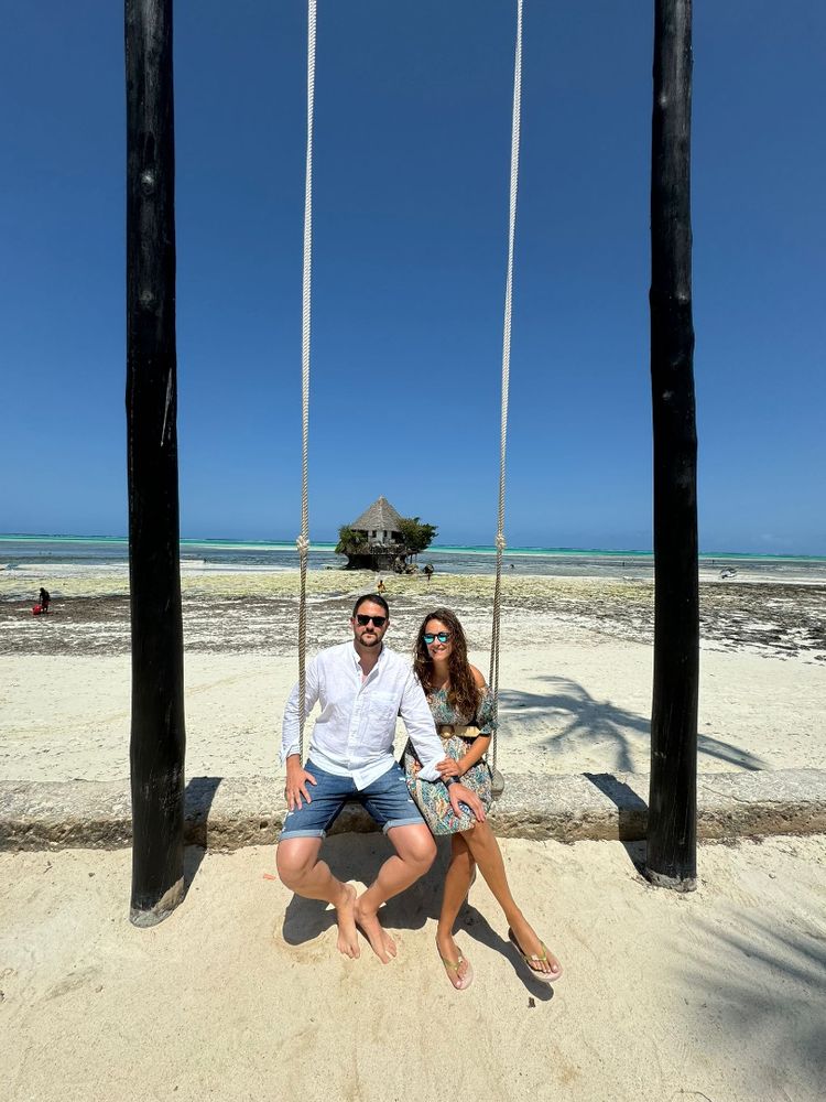Dos de nuestros viajeros sentados en un columpio a orillas del mar, con el restaurante The Rock a las espaldas, famoso por estar sobre una piedra en el mar.