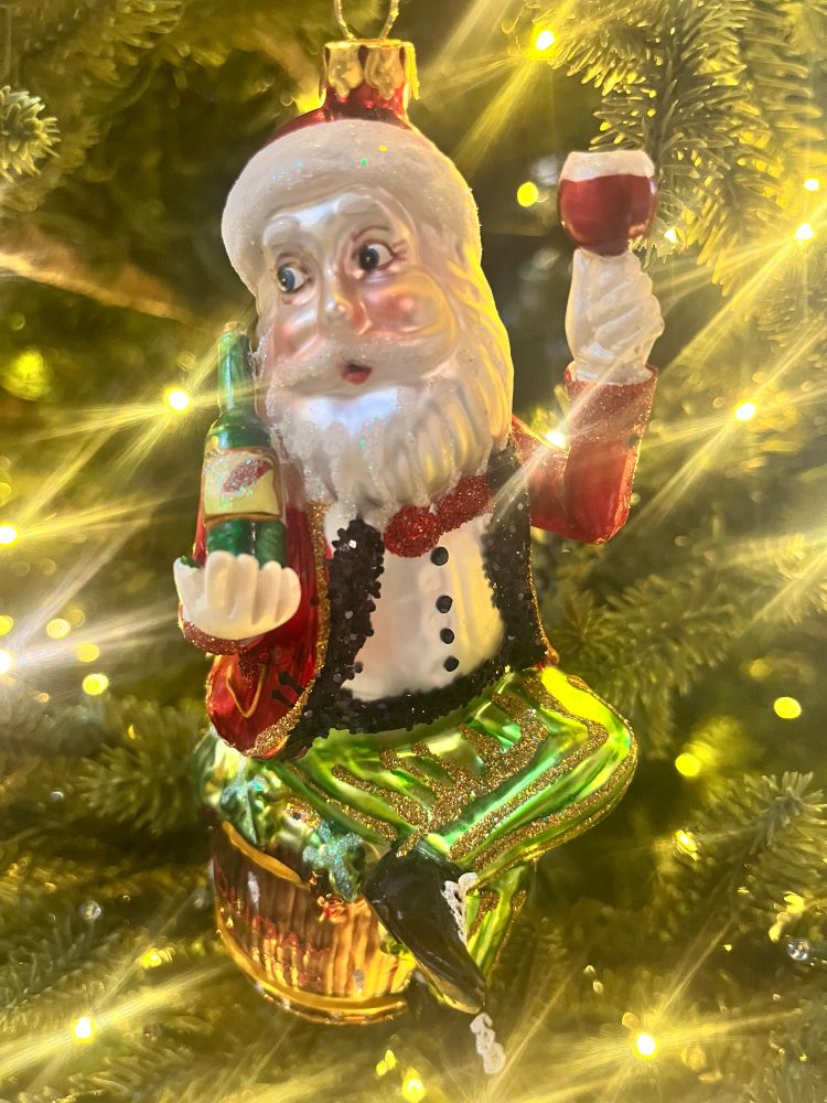 Ornament of Santa holding a bottle of wine in one hand a glass of red in the other sitting kinda diva like on a barrel