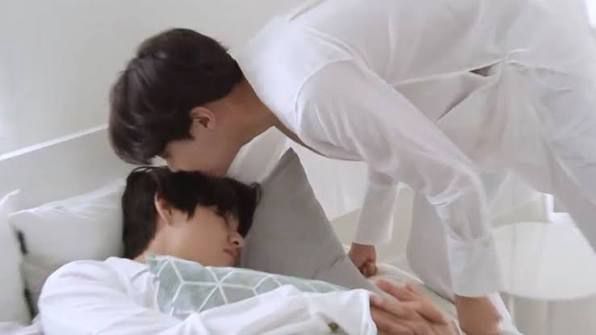 Hobi dressed in all white leans down to give a sleeping Tae a little smooch on his head 