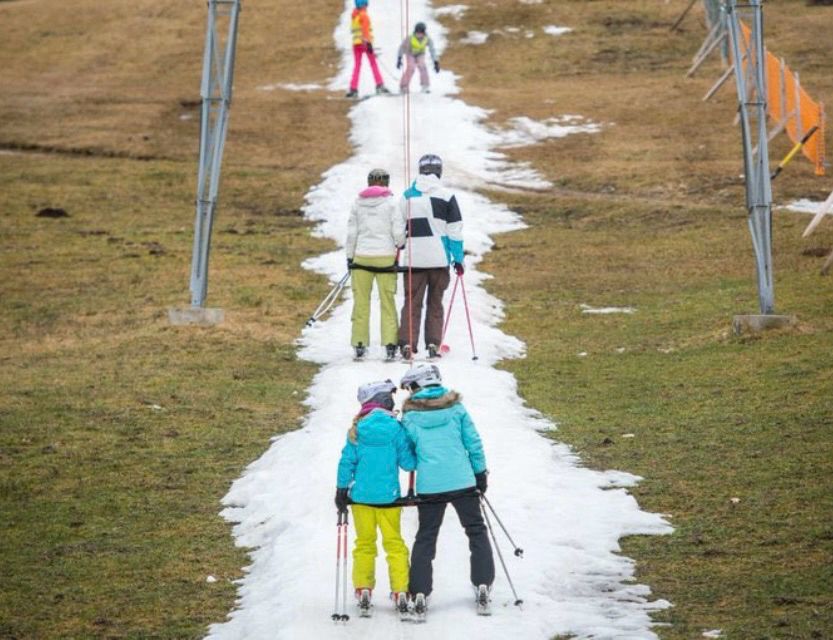 Wintersportler ohne Schnee auf einer schmalen, künstlich beschneiten Spur