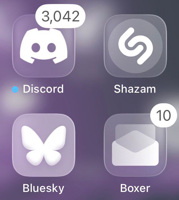 Application icons for Discord, Shazam Music Recognition, Bluesky, and Workspace ONE Boxer shown. Bluesky’s application icon standing out no longer following iOS 26’s Liquid Glass theming when it is set to a transparent icon, making the application icon look inconsistent and out of place. This image show the icon theme set to “Clear Light”