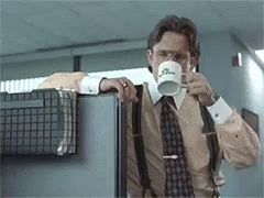 a man in a suit and tie is drinking a cup of coffee while leaning on a cubicle .