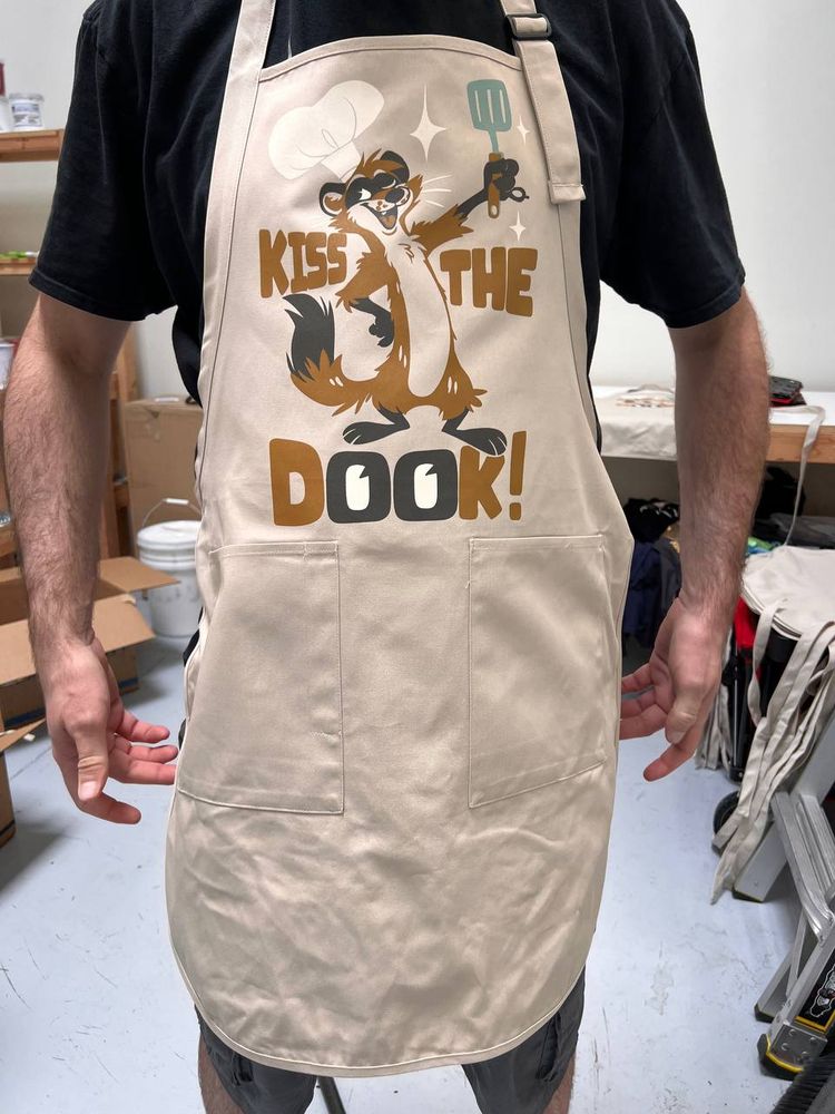 A cooking apron with a ferret on it and text that says "Kiss the Dook".