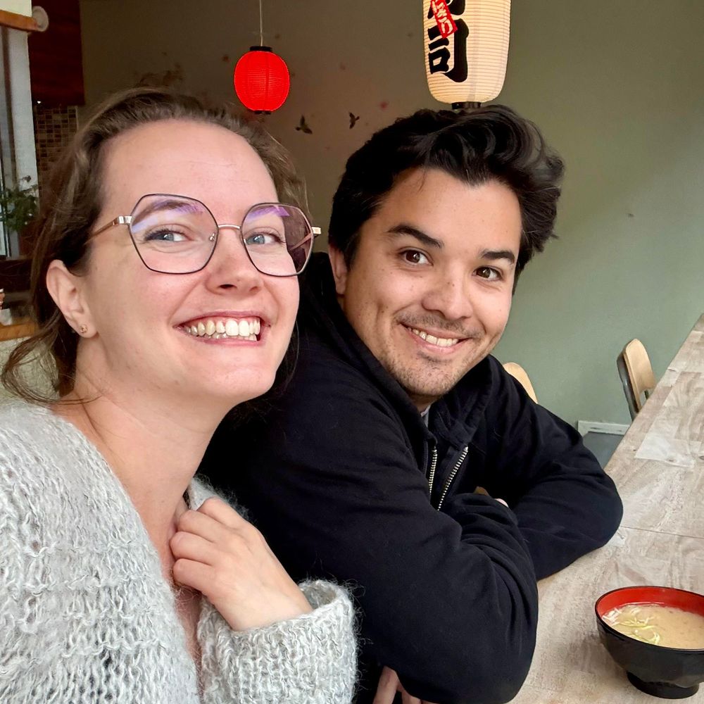 A man and a woman sit beside one another at a table and smile at the camera. They are Sofia and Cesar.