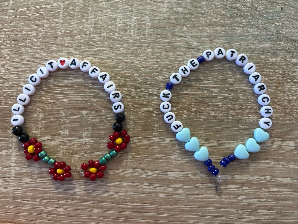 Ein Friendship Bracelet mit roten Blumen und „Illicit Affairs“ und eines mit blauen Herzen und „Fuck The Patriarchy“