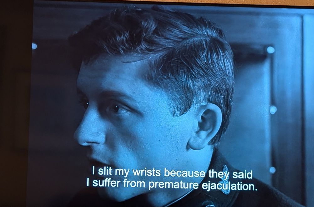 A black-and-white still from a movie of a young man's face. The subtitle reads "I slit my wrists because they said I suffer from premature ejaculation"