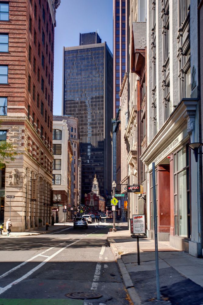 State street in Boston, two rows of modern buildings with the old state house near the end of a block, being towered over by a big, black building