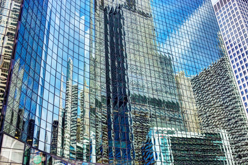 A curved wall of glass windows reflect the surrounding buildings with distortion