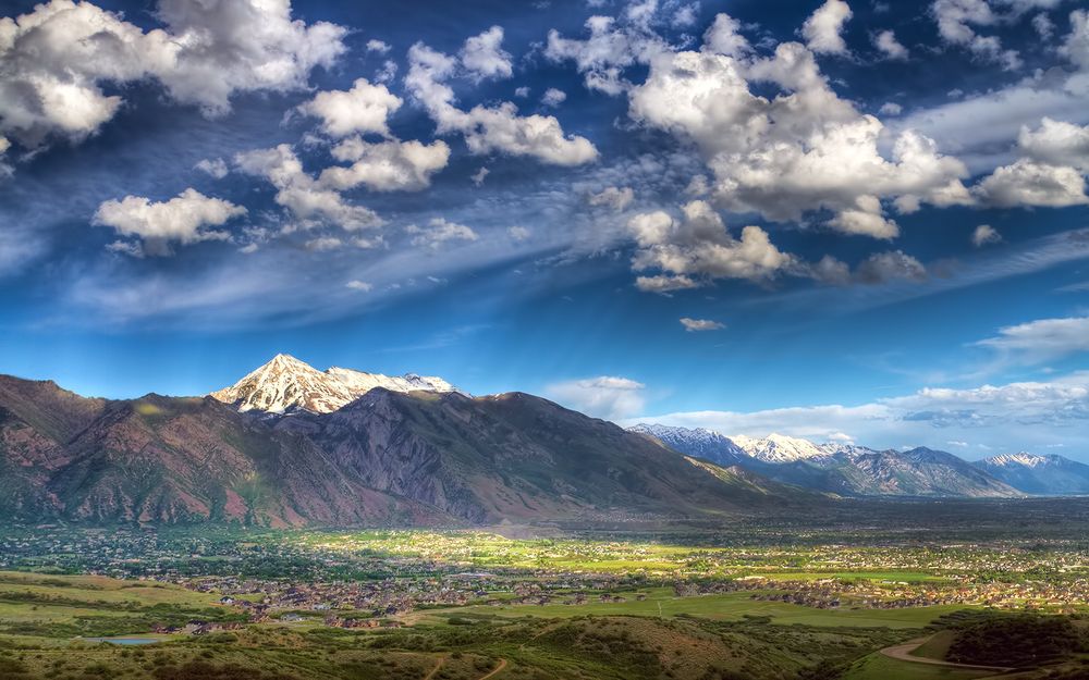 A valley is featured and foreground, mountains run the background from left to right, and even though it's only partly cloudy the sunlight dapples the scene 