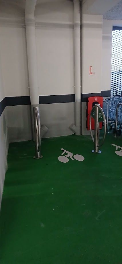Il y a deux arceaux vélo dans le parking couvert. Le sol est peint en vert et derrière l'un des arceaux on aperçoit un extincteur rouge.