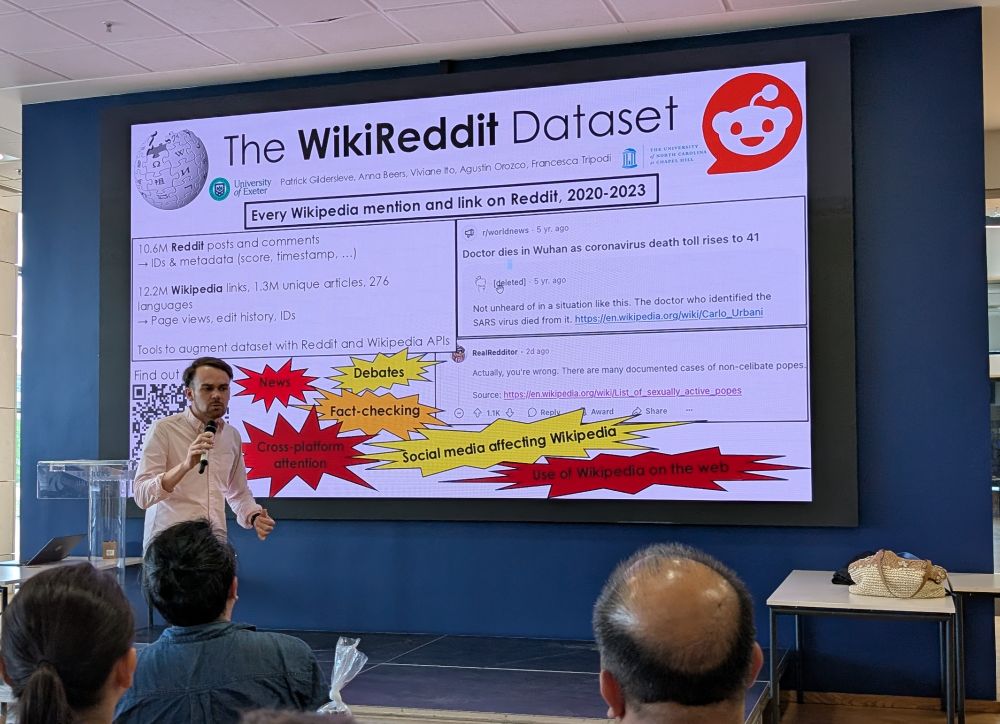 Presenter (Patrick Gildersleve) in front of a screen summarising the WikiReddit Dataset project. The slide describes it as "Every Wikipedia mention and link on Reddit, 2020-2023", includes some example usage, describes the scale of the dataset, and offers suggested use cases.