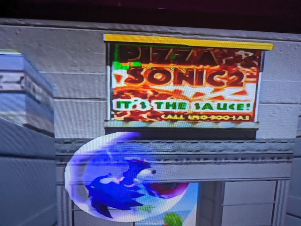 billboard in sonic adventure 2 saying "PIZZA SONIC2 IT'S THE SAUCE!"