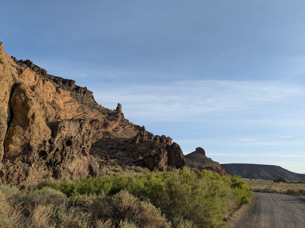 A rocky mesa, brush in front, blue sky above