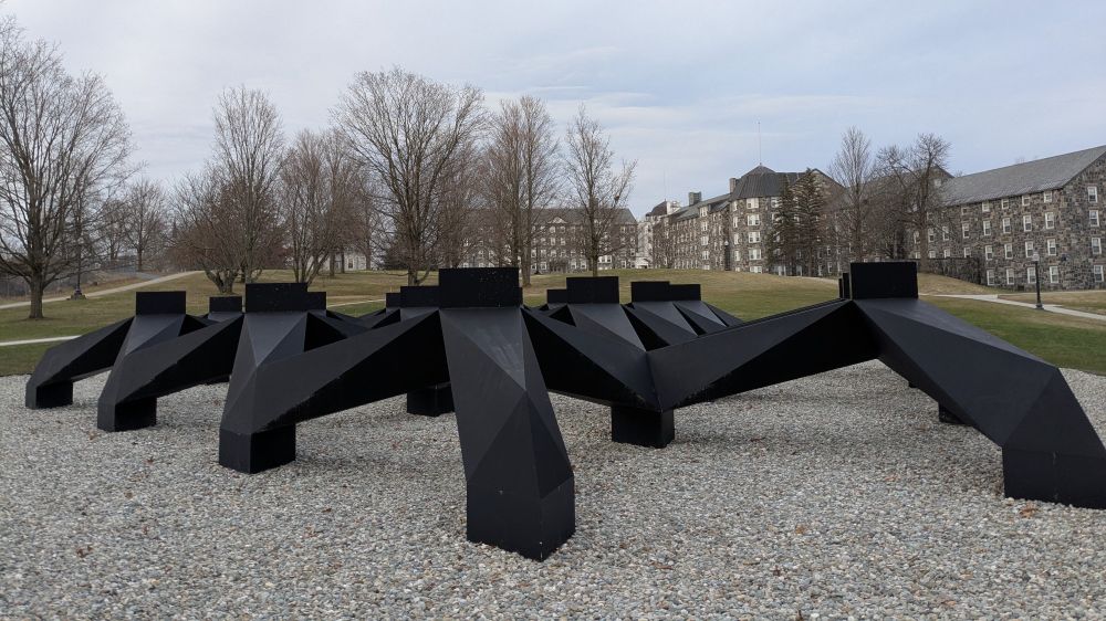 Public art, looking like maybe a bunch of huge metal claws sitting on the ground, with a college quad behind
