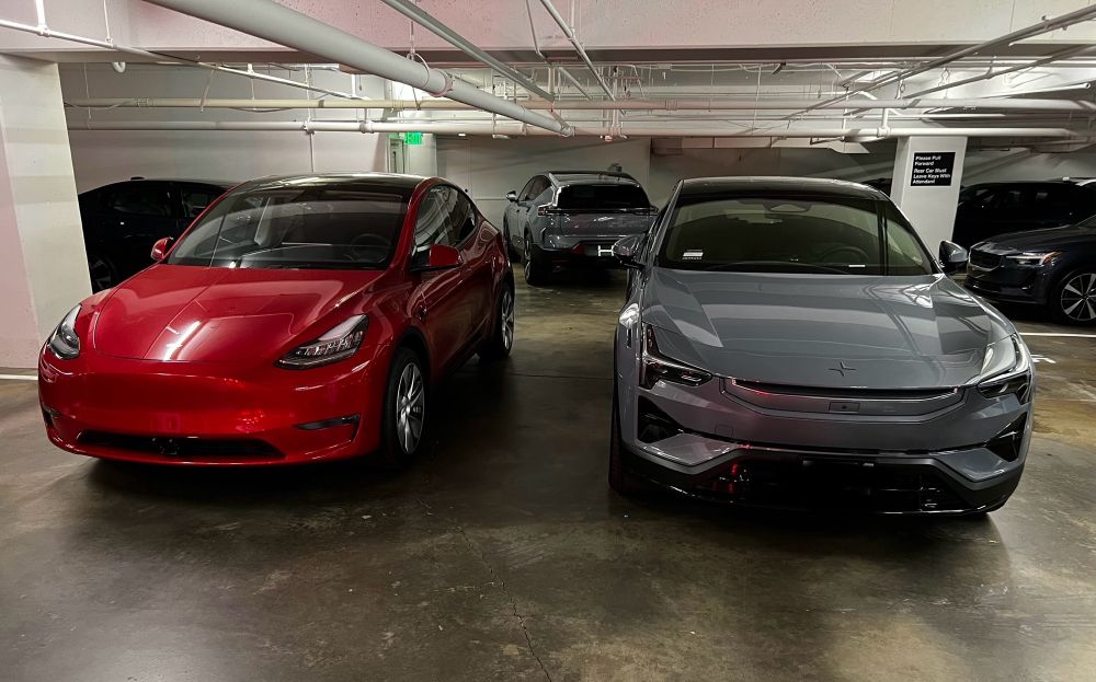 Two cars side by side - front views. Red Tesla Y on left and gray Polestar 3 on right.