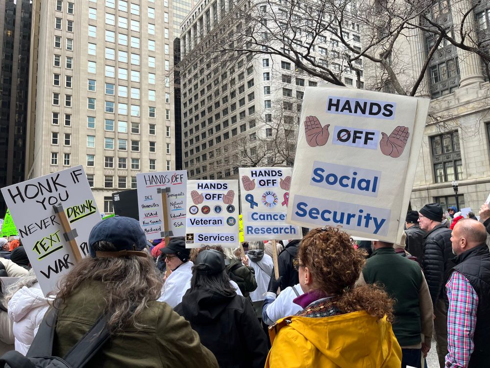 Protesters hold signs bearing messages like “hands off social security”