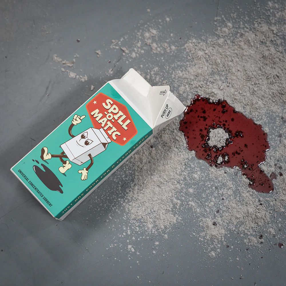 A carton of spill-o-matic on a garage floor next to a spill with the product spread around it.