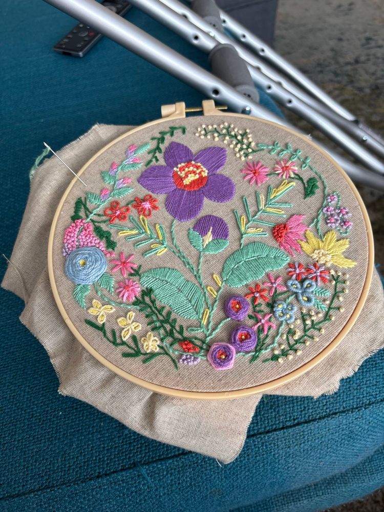 A floral embroidery with cotton thread on undyed fabric. Crutches in the background. 