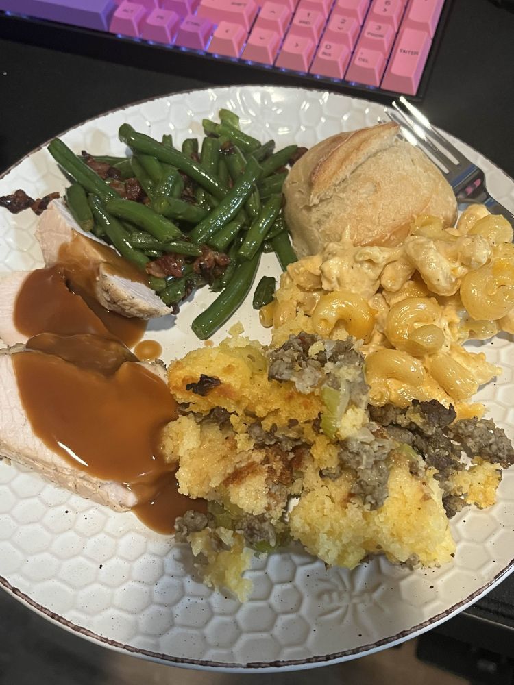 Thanksgiving plate with turkey and gravy, cornbread stuffing with sausage, Mac and cheese, green beans, and a dinner roll.