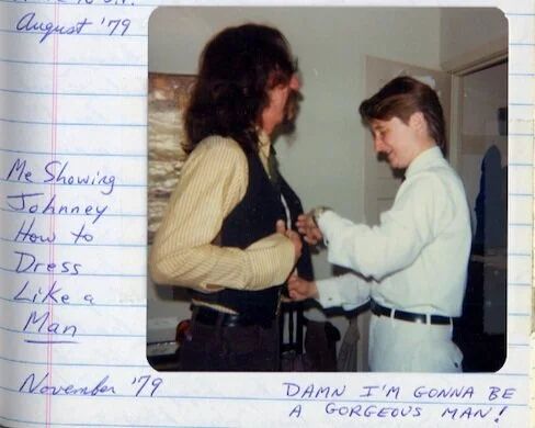 A photo of Lou Sullivan (right) helping another man (presumably Johnney, left) get dressed in formal attire.
There's writing in pen that reads (from left to right):
"August '79.
Me showing Johnney How to Dress Like a Man ("man" is underlined).
November '79.
DAMN I'M GONNA BE A GORGEOUS MAN!"