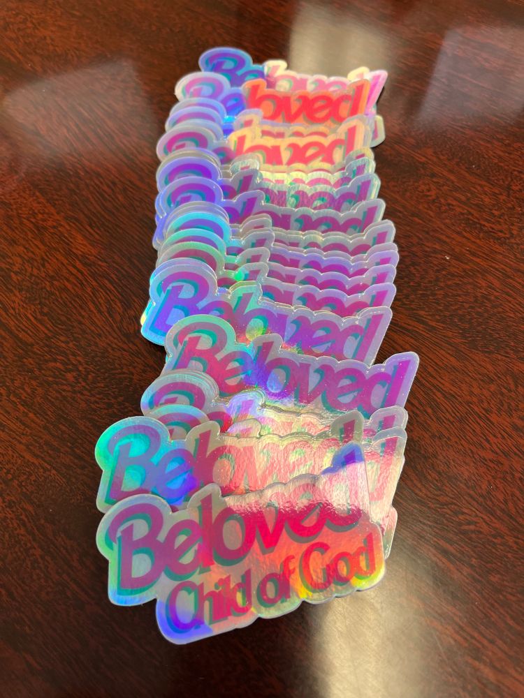 Holographic sticker that says “Beloved Child of God” in a pink, Barbie-inspired typeface