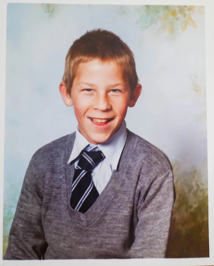 George as a child in his school uniform, cheekily smiling at the camera