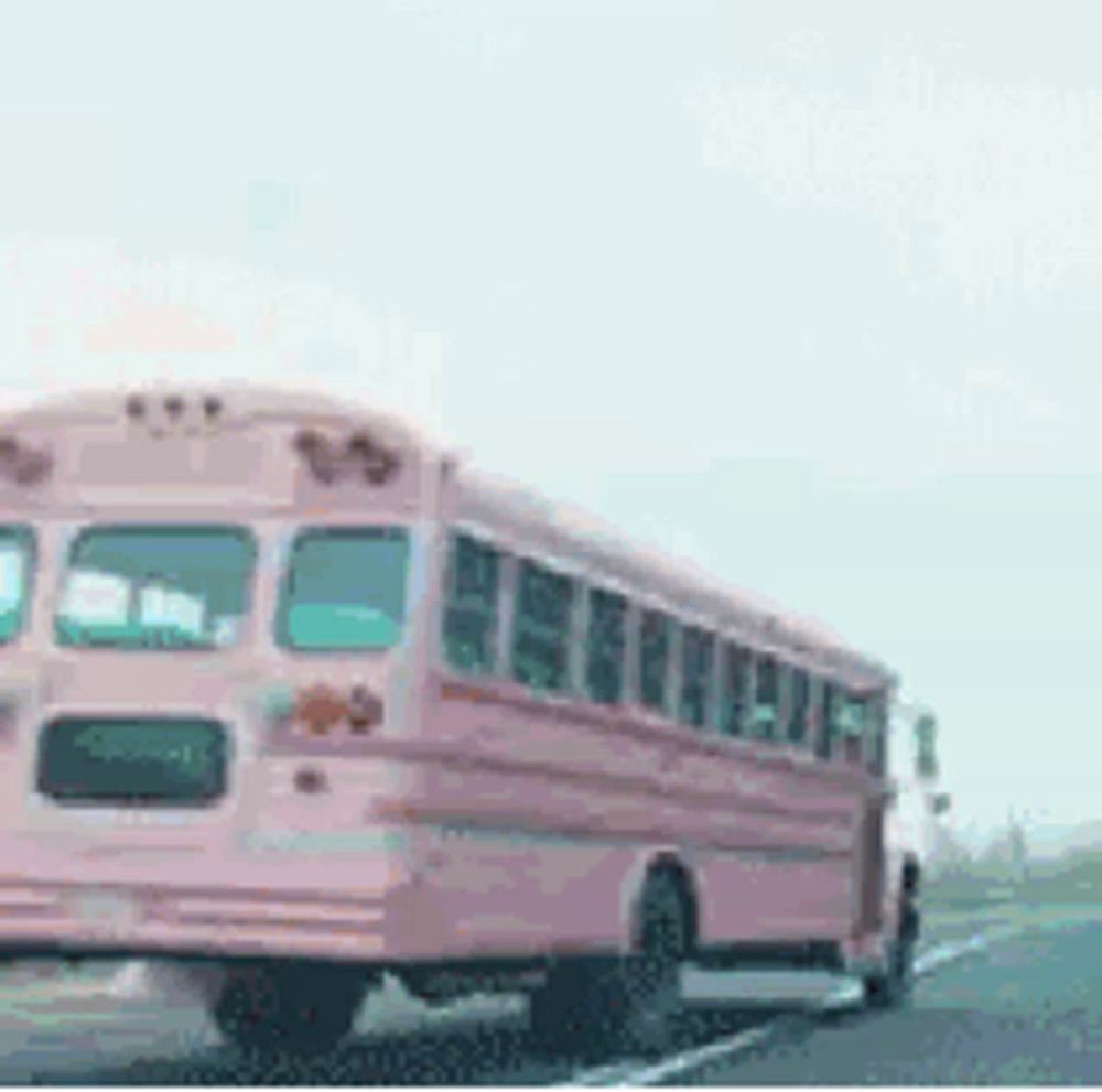 a pink school bus is driving down the highway .