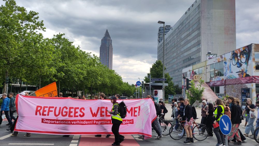 Demo, im Vordergrund Refugees Welcome Transpi, im Hintergrund der Messeturm.