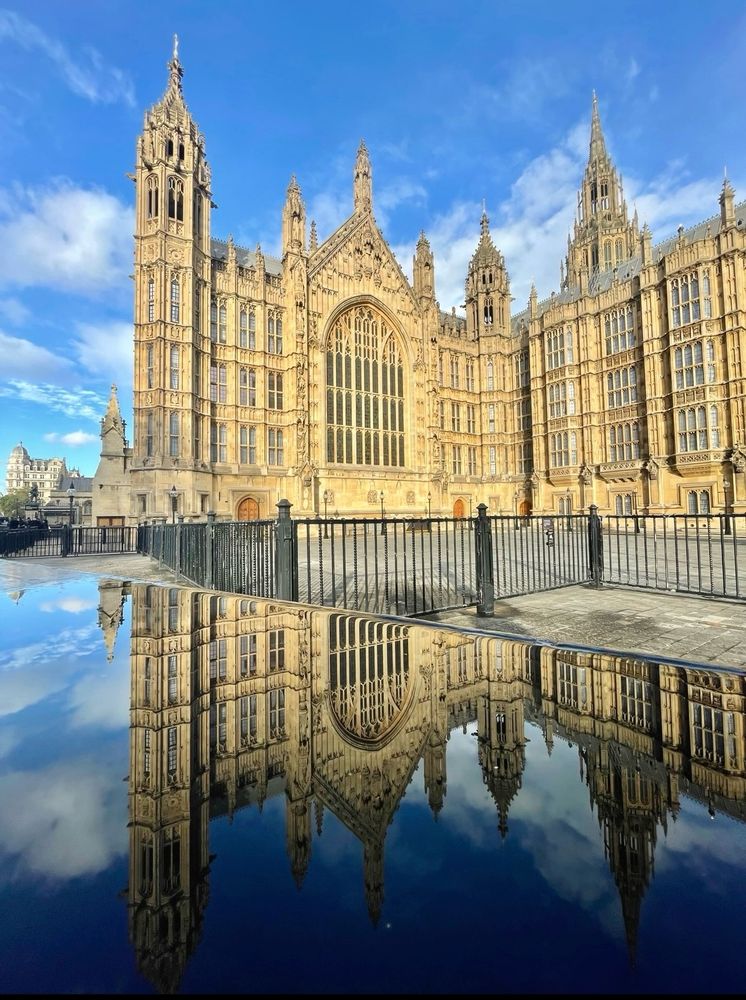 A photograph of the Houses of Parliament reflected in a small puddle on a barrier 
