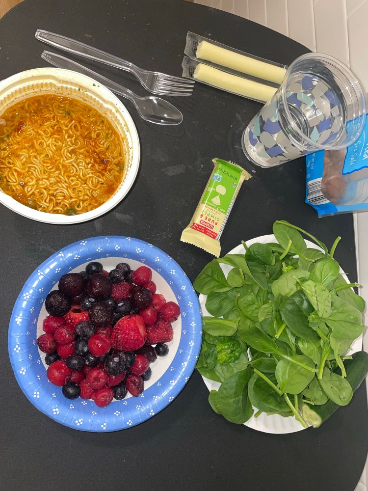 Ramen, berries, spinach, granola bar, almonds, cheese sticks, and water on a black table