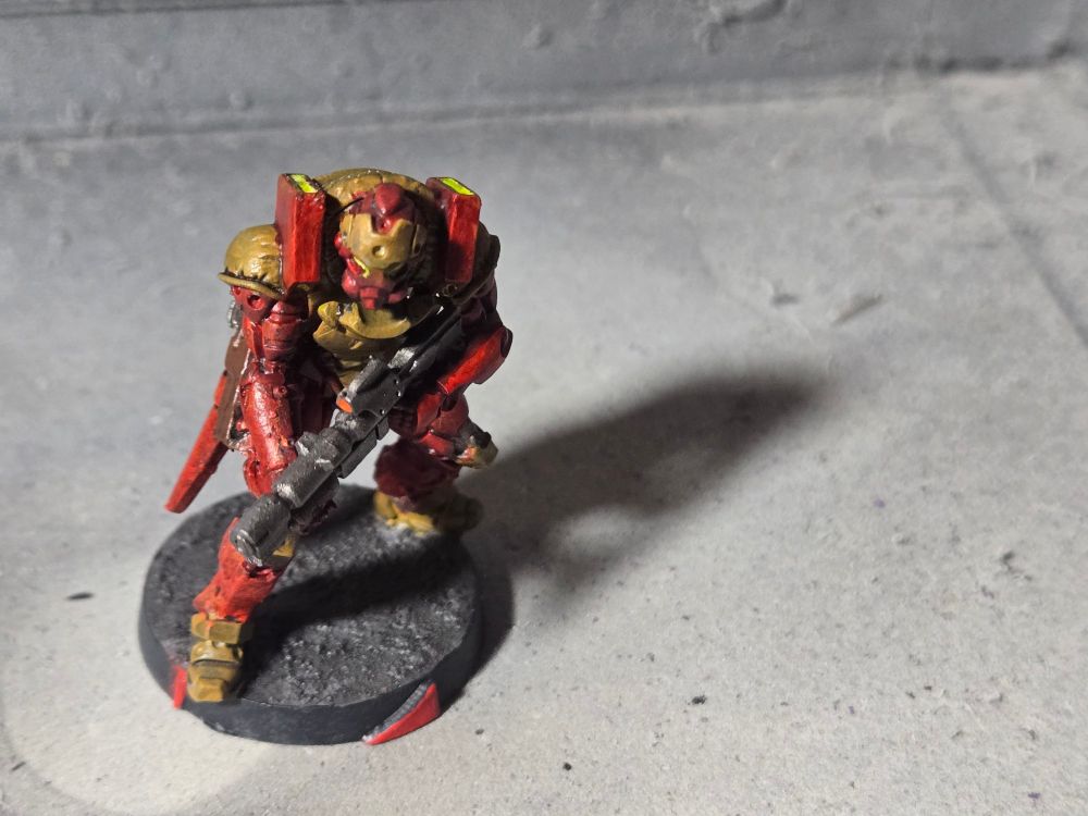 Asawira armed with a spitfire. Armor is tan on the chest, shoulders, knees, feet, and on the helmet above the face. The rest is blood red. The spitfire is gunmetal.