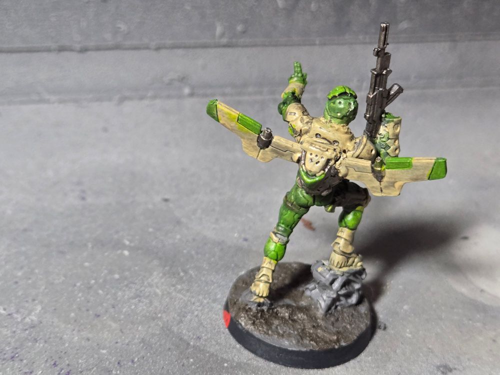 The back of the Ragik. His jet pack is sand colored with green accents and gunmetal jets. The ground is gray and brown.