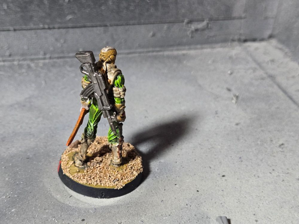 The back of the red faced Fiday. A gunmetal rifle is on his back, the butt sticking up over his left shoulder. A metallic red dagger can now be seen in his left hand.