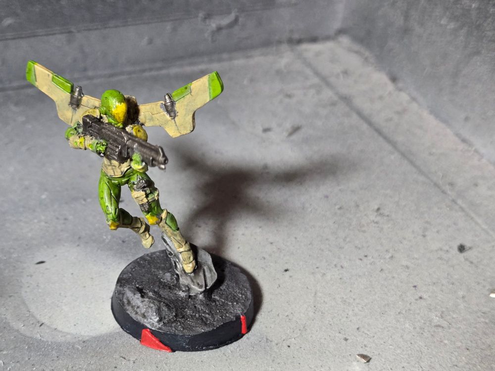Hassassin Ragik jumping off of a tactical rock and aiming forward with a boarding shotgun. Armor is light sand and light green. Helmet is light green with a yellow face plate.