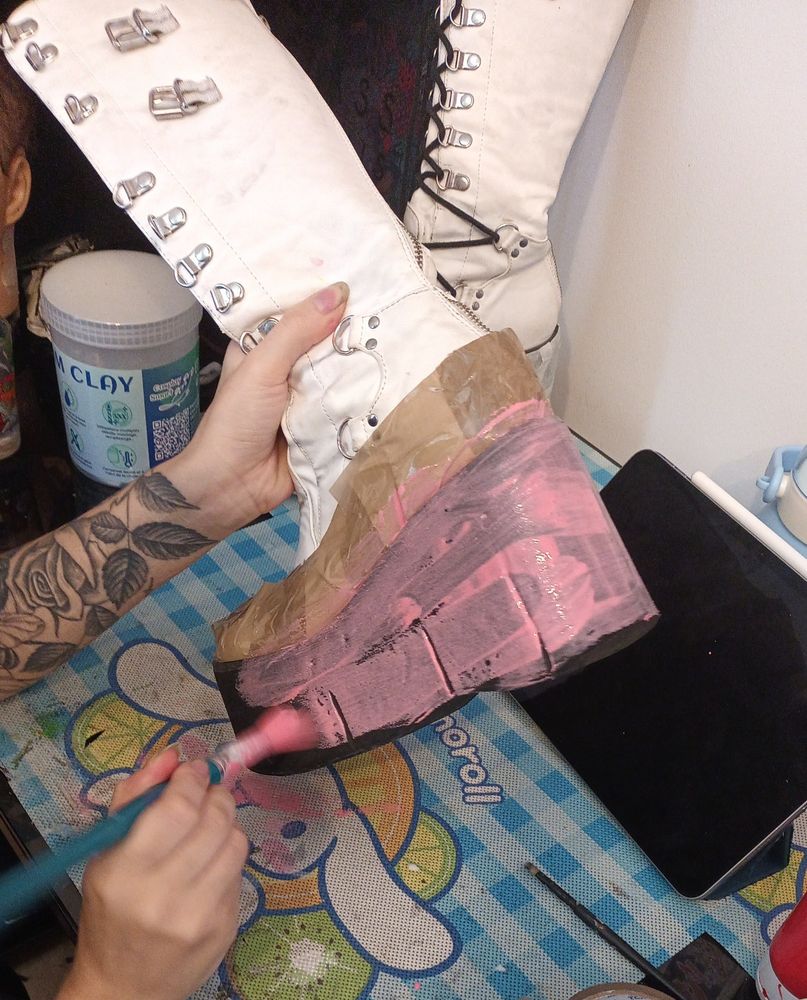 someone painting pink over a the black sole of a white platform boot. 