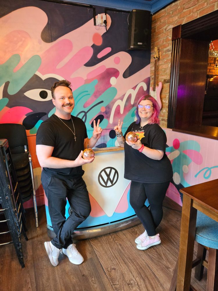 James and Rosie in Archie's in Newcastle, near the law school of Uni of Northumbria. The decor is cute pink, blue, and white pastel graffiti, and the DJ booth is in the shape of a VW camper van's front bonnet. Both Rosie and James look cute, have gay disco ball cocktails, and are giving standard peace signs